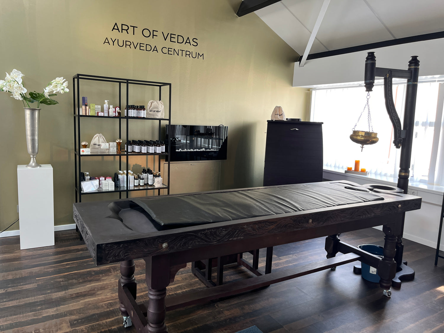 Art of Vedas Ayurveda Centrum in the Netherlands - Panchakarma treatment room with traditional wooden massage table, Shirodhara equipment, and Ayurvedic products