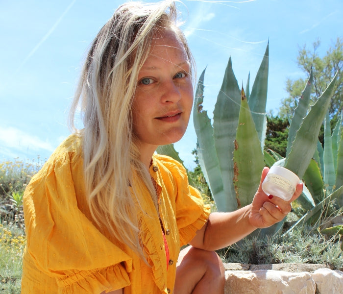 Woman holding Art of Vedas natural face cream outdoors in botanical garden - Ayurvedic moisturizer for radiant and healthy skin